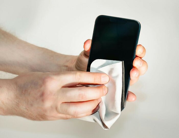 Person cleaning a smartphone screen with a cloth, focusing on common hygiene habits.