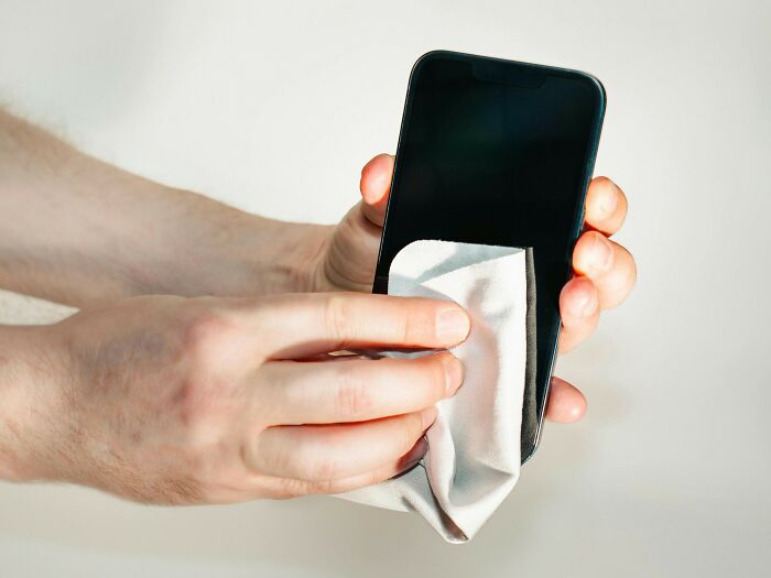 Cleaning phone screen with cloth, addressing everyday people's habits and cleanliness concerns.