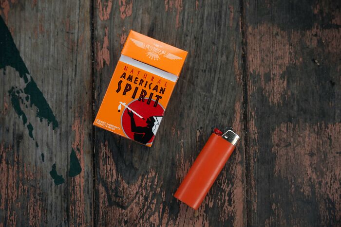 Packet of Natural American Spirit cigarettes and an orange lighter on a wooden surface, highlighting shocking cultural differences.