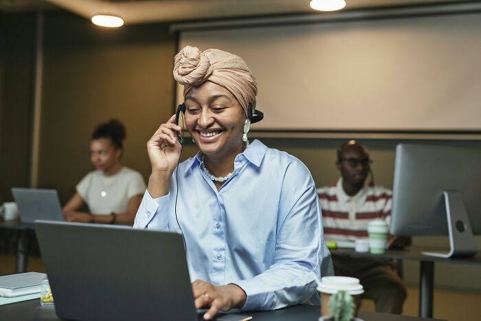 Woman in customer service role, smiling with headset, working on a laptop.