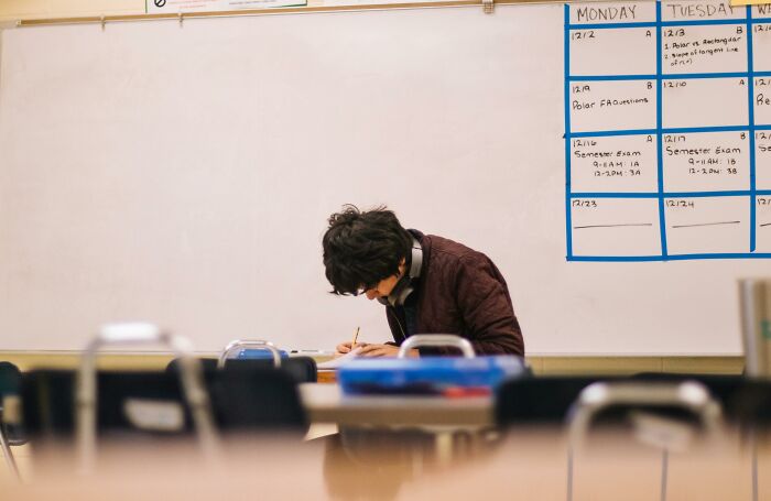 Student alone in a classroom, writing at a desk, illustrating harsh realities about life and education challenges.
