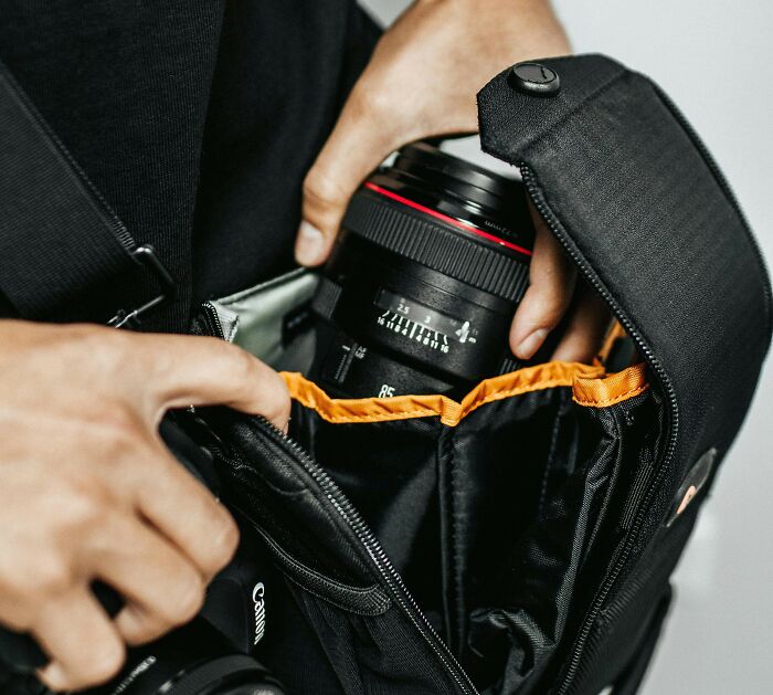 A person places a durable camera lens into a black bag with orange lining.