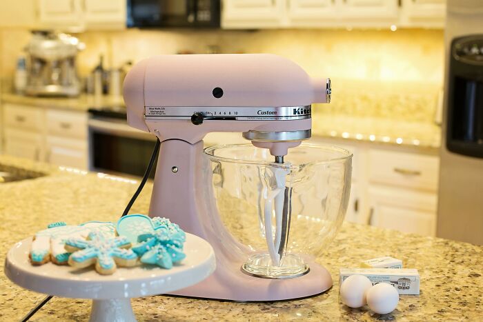 Pink stand mixer on a kitchen counter, showcasing durable design next to decorated cookies and baking ingredients.