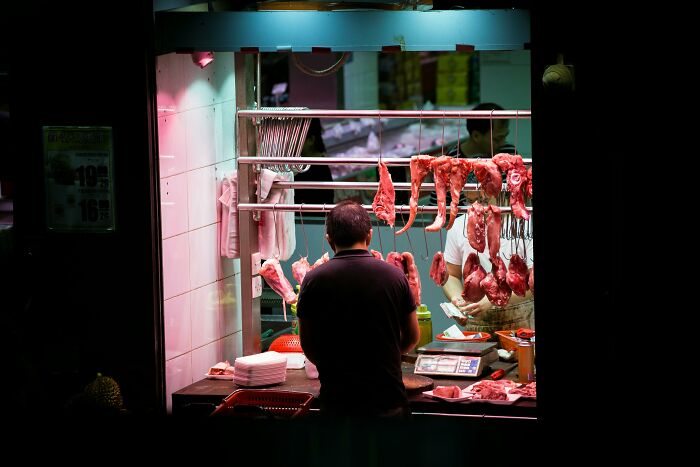 Butcher shop with hanging meat, where two people skillfully prepare cuts under a neon light, reflecting deeply weird vibes.