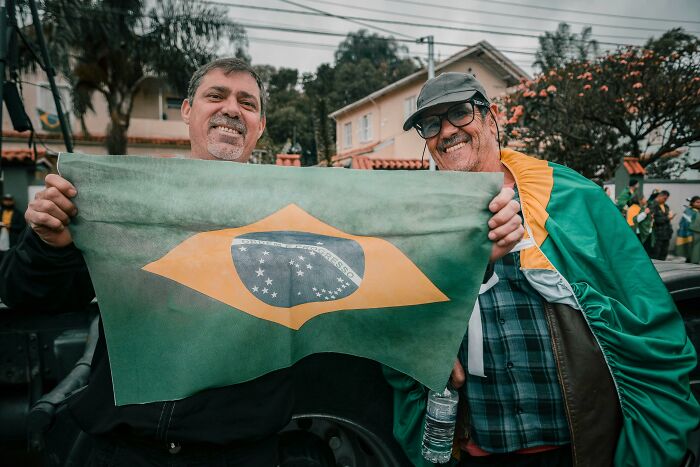 Two men happily holding a Brazilian flag outdoors, illustrating hilarious overheard conversations.