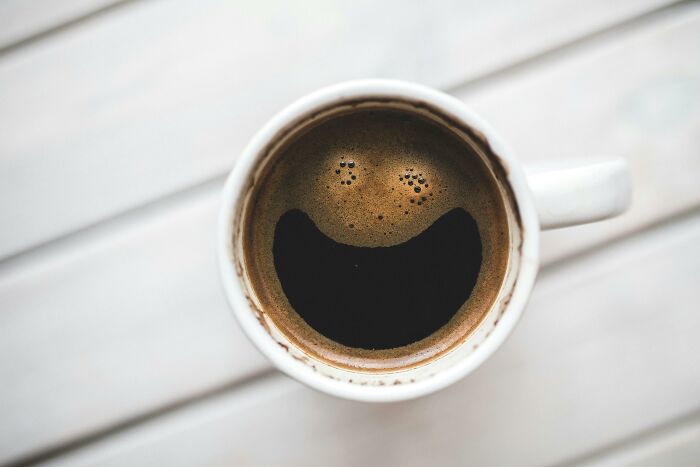 A coffee cup with froth forming a smiling face, creating a lighthearted mic drop moment on a wooden surface.