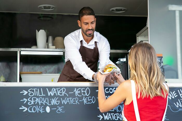 Food vendor handing a sandwich to a woman at a food truck counter.