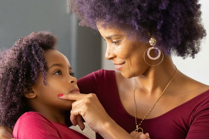 Mother and child with curly hair, wearing matching burgundy tops, sharing a tender moment.