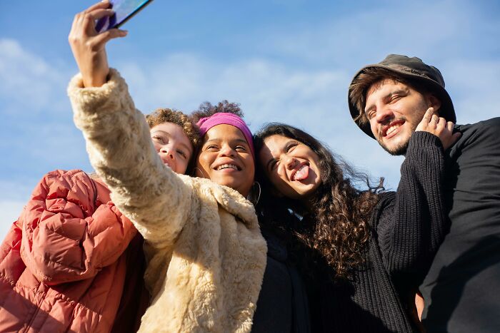 Group of four friends taking a selfie outdoors, smiling and cheerful, embracing brilliant life hacks for joyful living.