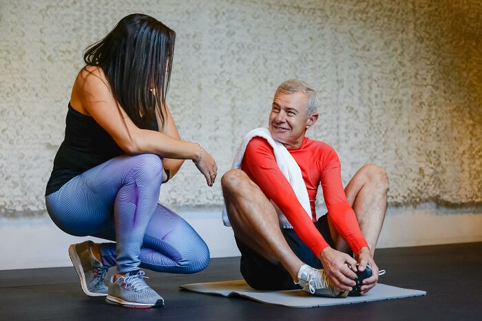 Man and woman discussing fitness myths during a workout session, with the man stretching on a mat.