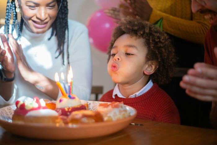 Child blowing out birthday cake candles, surrounded by family clapping, representing common people's habits.