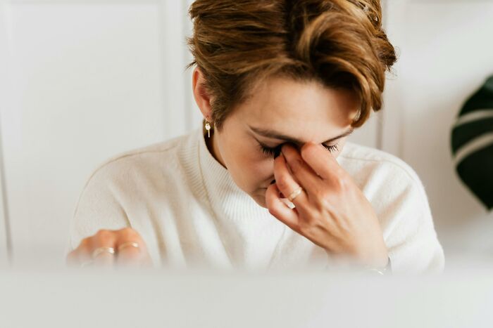 A person in a white sweater sits with closed eyes, conveying stress, related to therapists and changing mindsets.