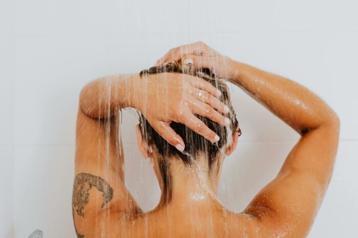Person under running shower, hands on head, showing love and care for self.