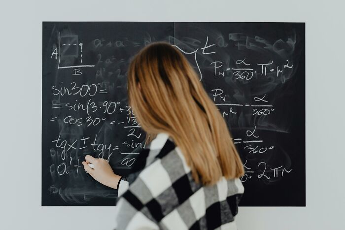 Person writing on a chalkboard filled with math equations, embodying a scene of overheard conversations in an academic setting.