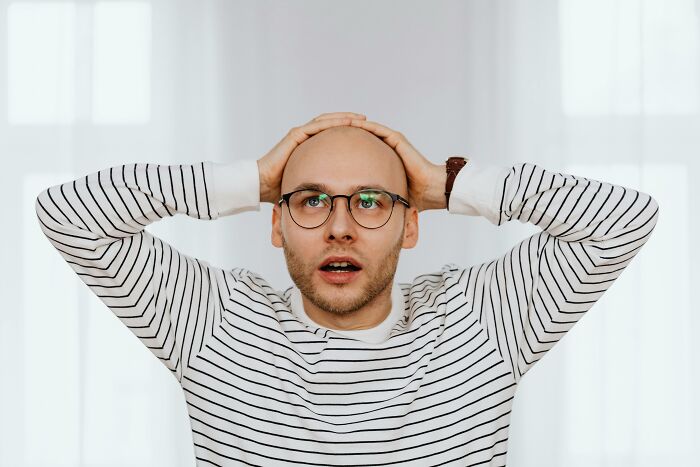 Man with glasses and striped shirt holding his head, illustrating reactions to bizarre things real men don't do.
