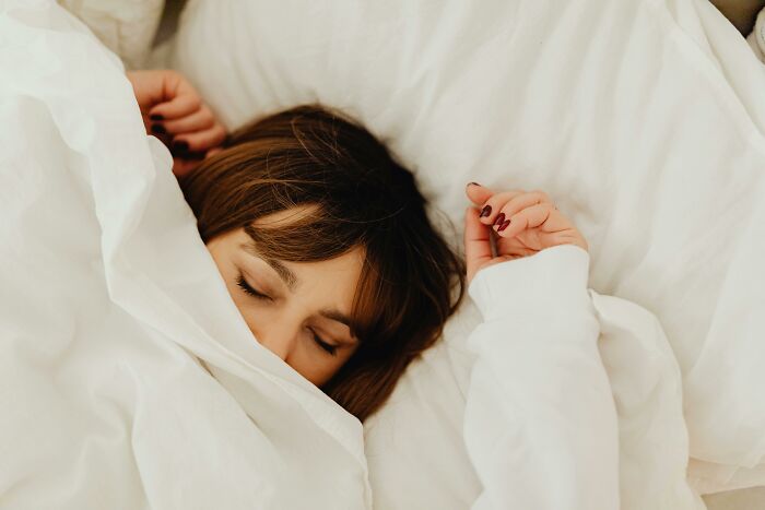 Woman peacefully sleeping under white sheets, illustrating an eye-opening moment of rest and tranquility.