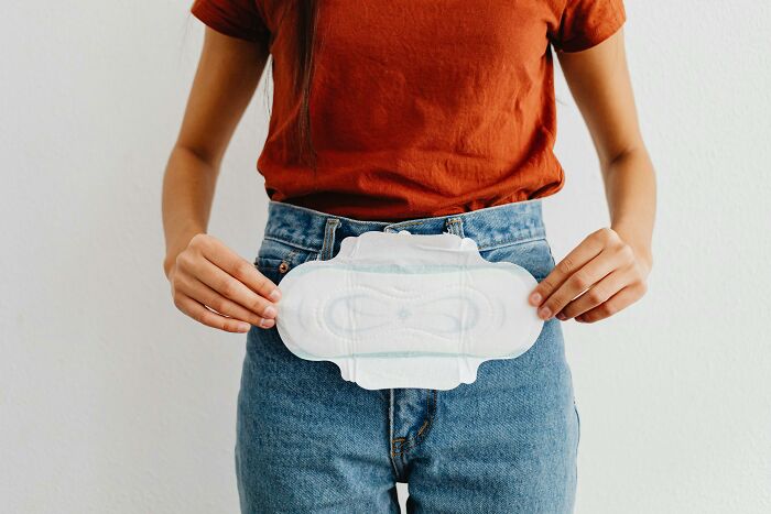 Woman holding a sanitary pad in front of her waist, illustrating health and comfort benefits of not going to the office.