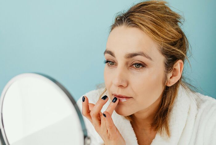 Woman in a white robe applying lip balm, demonstrating common hygiene habits.