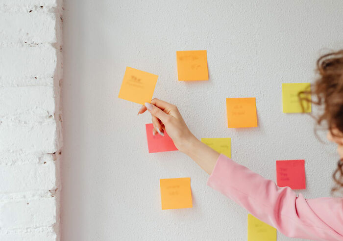 Hand with pink sleeve placing sticky notes on wall, concept of revenge planning.