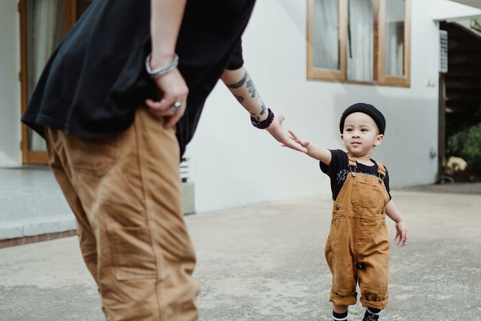 A young child and adult holding hands outdoors, illustrating concepts of real men and parenting in a casual setting.