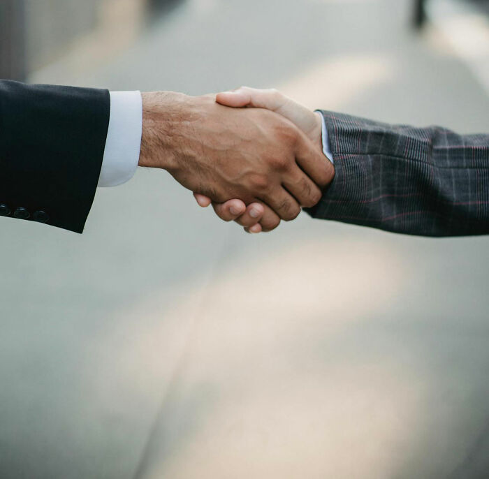 Two people in business attire shaking hands, symbolizing power dynamics and potential revenge.