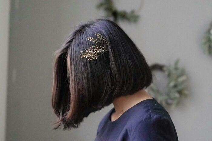 Woman with bob haircut and gold hair accessory, modeling 2025 trends in a minimalist setting.