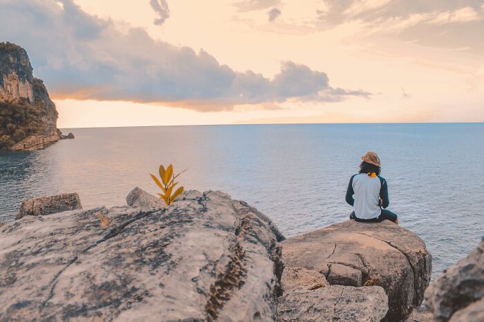 Person sitting on rocks overlooking the ocean at sunset, capturing the essence of 2025-Trends in travel and solitude.
