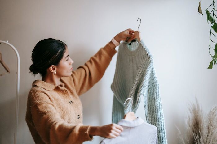 A woman decides between two sweaters, illustrating frugal shopping choices.