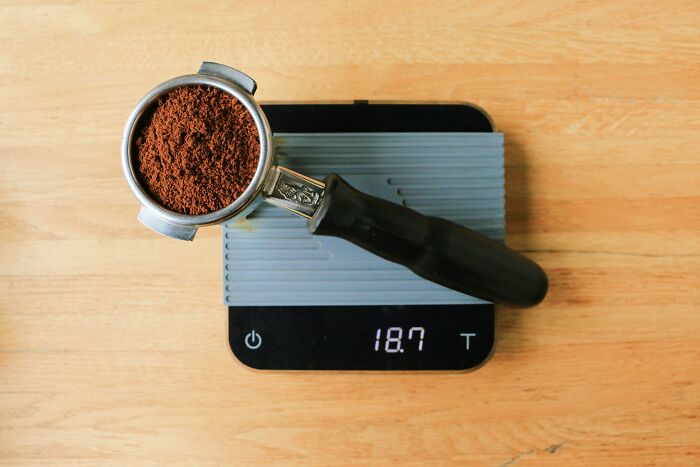Portafilter with ground coffee on digital scale, illustrating multipurpose kitchen items for minimalism.
