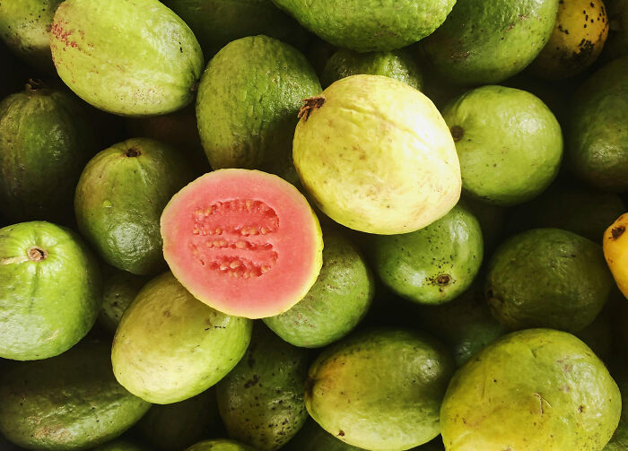 Guavas with one cut open, showcasing the vibrant pink interior, highlighting health-boosting fruits.