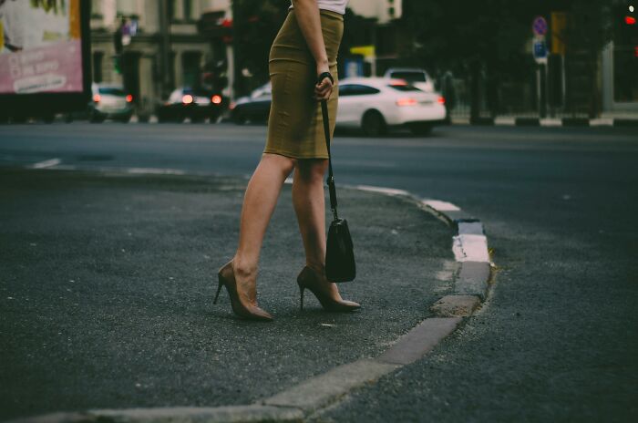 Woman in high heels standing at city street corner, highlighting cultural differences in fashion choices.