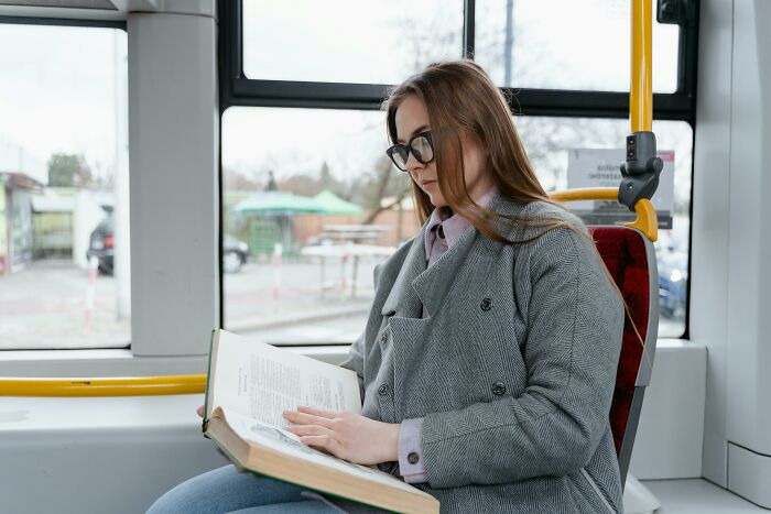 Person reading on a bus, possibly ignoring social rules by focusing on a book in transit.
