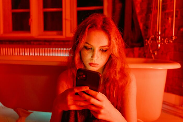 Woman in red lighting looking at smartphone, illustrating adult people facing harsh life lessons.