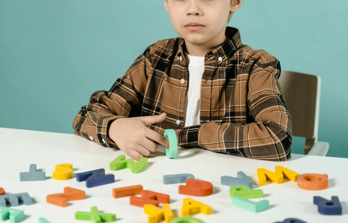 Child with wooden letters on a table, wearing a plaid shirt, in a blue and beige setting. Creepiest family sayings theme.