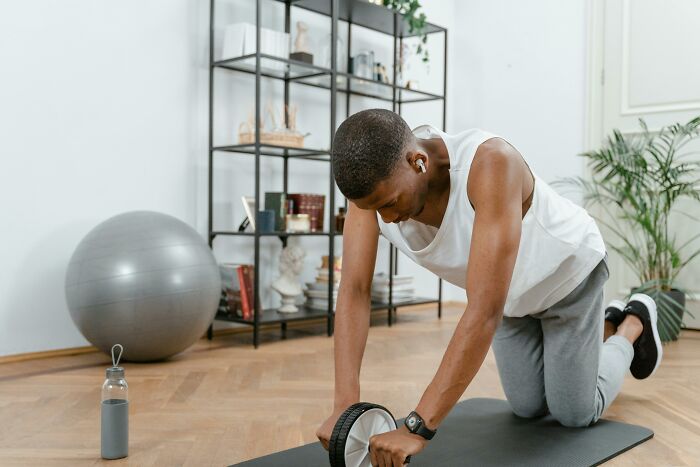 Person using an ab roller in a home gym, featuring self-paying-products like a yoga mat and exercise ball.