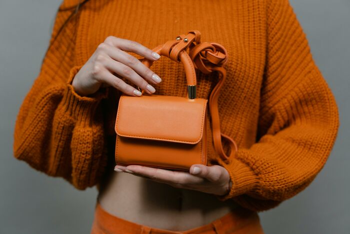 Person in orange sweater holding a small orange handbag, showcasing recent fashion trends people dislike.