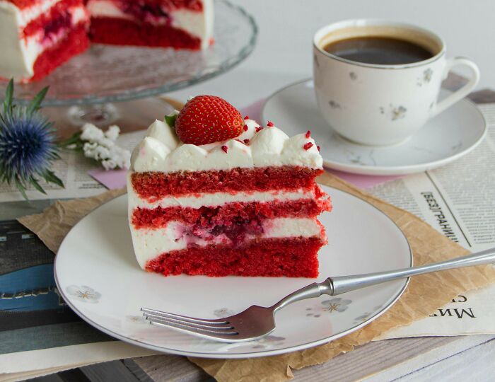 Slice of red velvet cake with a strawberry beside a cup of coffee, ideal for a simple Valentine's gift.