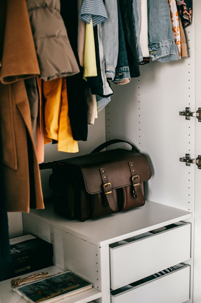 Organized closet with folded clothes and a leather satchel, showcasing life improvement through tidiness.
