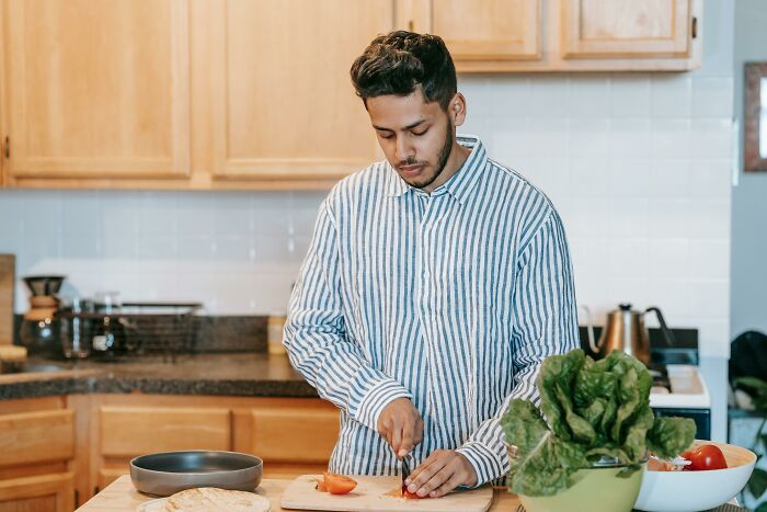 Man in striped shirt preparing food in kitchen, illustrating unusual things real men don’t do in daily life.