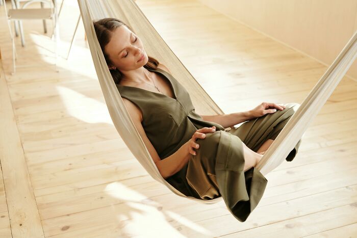 Relaxation trends 2025: Person in a hammock wearing an olive-green dress, sitting in a sunlit room with wooden floors.
