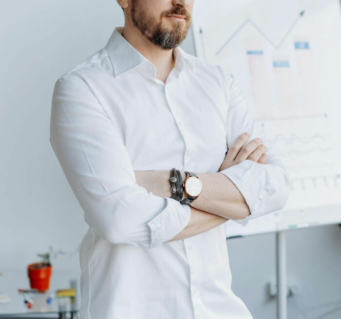 Man in white shirt with arms crossed, standing near a chart, conveying power dynamics.