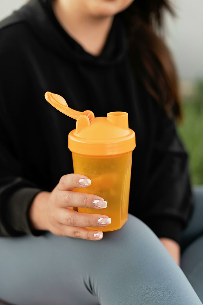 Person holding orange cup with lid, representing life-improving items from a viral discussion thread.