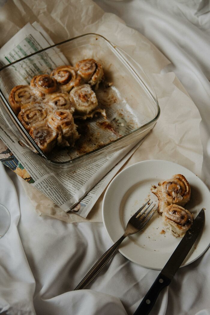 Cinnamon rolls in a glass dish on a bed, with one roll on a plate and cutlery, illustrating life improvements.