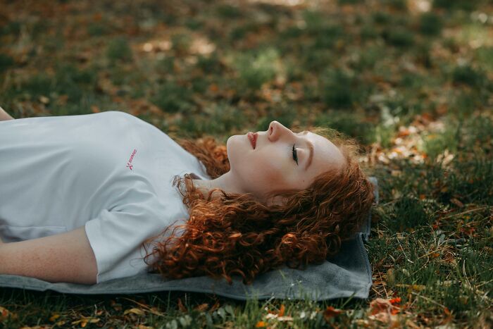 A woman with curly red hair lies peacefully on grass, reflecting childfree lifestyle benefits.