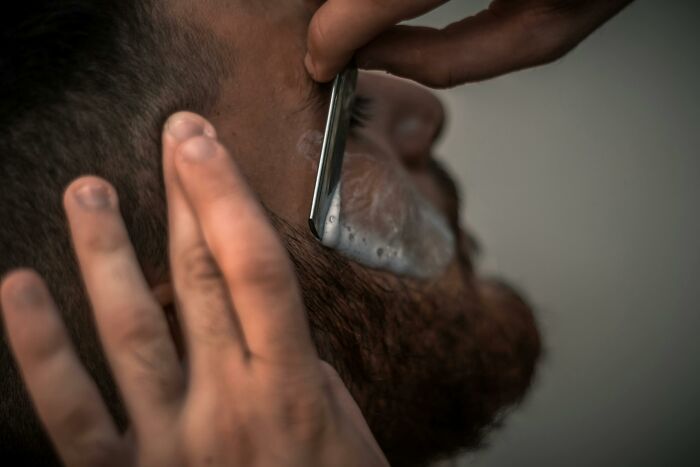 Man receiving a traditional straight razor shave, highlighting cultural differences in grooming practices.