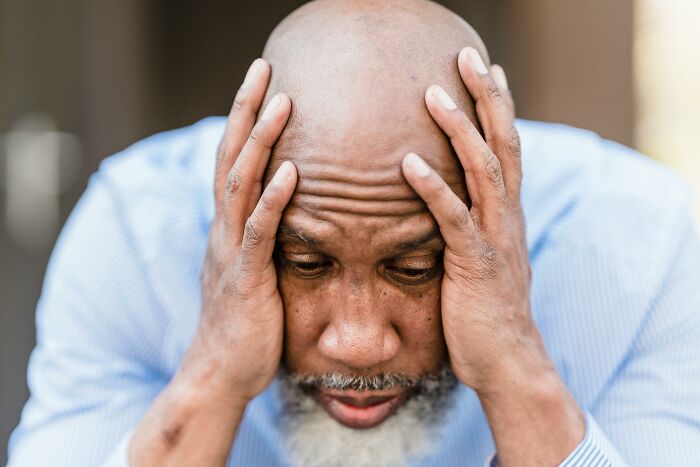 A man looking stressed, holding his head with his hands, signifying adult harsh life lessons.