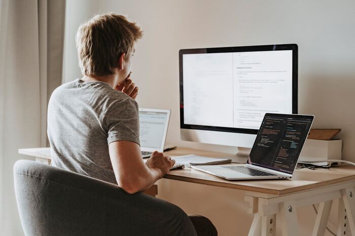 Person working at a desk with multiple screens, focused on coding, possibly planning revenge on someone in power.