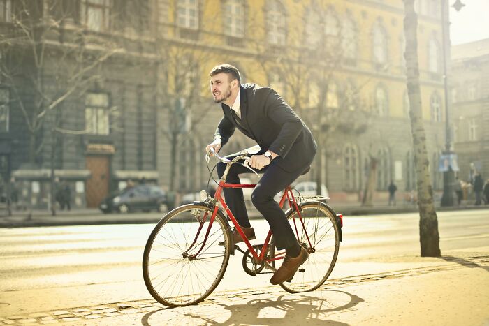 Man in a suit riding a bicycle on a sunny street, concept of self-paying-products through eco-friendly transportation.