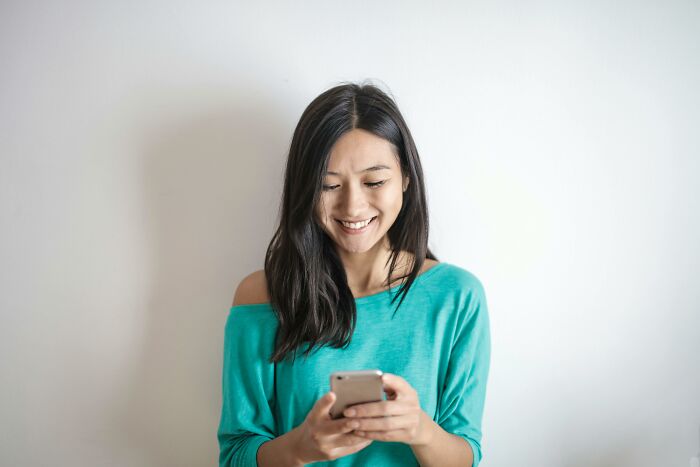 Smiling woman, wearing a teal shirt, looking at smartphone, possibly reflecting on social rules people ignore.