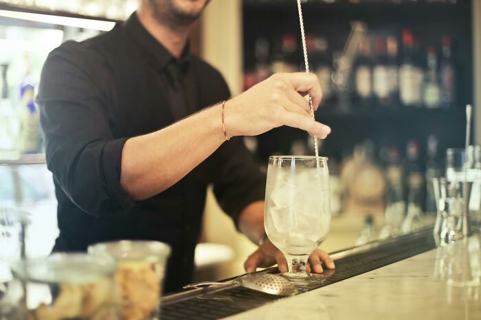 Bartender stirs a cocktail with ice at a bar, creating a relaxed ambiance, representing mic-drop-moments in mixology.